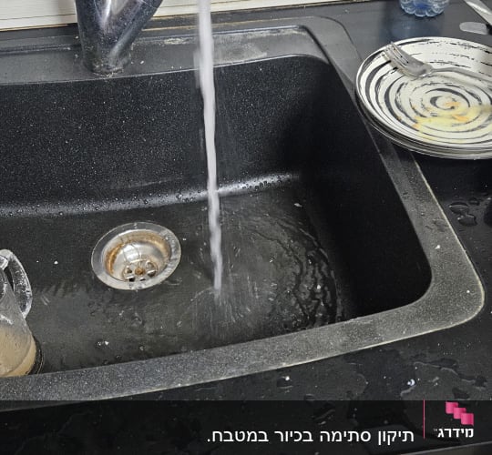 ברז מים זורם בכיור מטבח עם כלים מלוכלכים